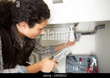 female plumber sitting on the floor fixing a bathroom sink Stock Photo