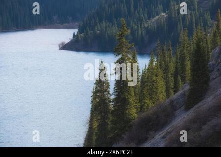 Forest slopes of a mountain lake with blue water. Lake Kulsay or Kolsai in Kazakhstan Stock Photo