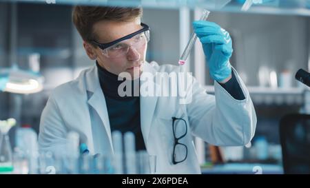 Modern Medical Laboratory: Young Caucasian Male Research Scientist Checking Mixed Chemical Liquids in a Test Tube. Microbiologists Conducting Biotechnology Research. Portrait Shot Stock Photo