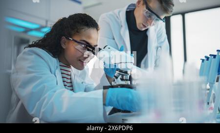 Modern Medical Research Laboratory: Portrait of Black and Caucasian Young Scientists Using Microscope, Digital Tablet, Doing Sample Analysis, Talking. Diverse Team of Specialists work in Advanced Lab Stock Photo
