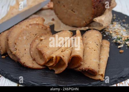 Seitan shaped and cooked in ham press, sliced on slate board. Vegan protein, plant based alternative to meat. Stock Photo