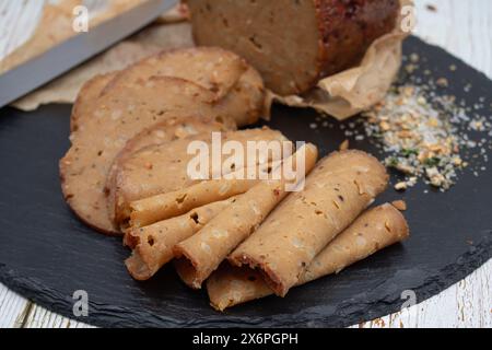 Seitan shaped and cooked in ham press, sliced on slate board. Vegan protein, plant based alternative to meat. Stock Photo