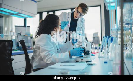 Modern Medical Research Laboratory: Portrait of Two Young Scientists Microscope, Doing Sample Analysis, Talking. Diverse Team of Multi-Ethnic Specialists work in Advanced Lab Stock Photo