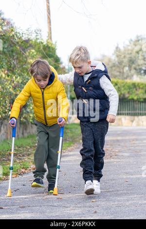 Two 8 year old boys walking together, one on crutches Stock Photo