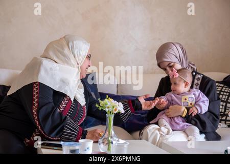 Mother and grandmother are playing with baby wearing beautiful clothes celebrating and enjoying their moments with children Stock Photo
