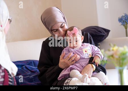 Mother holding kid looking at the camera feeling love with her baby wearing beautiful clothes celebrating eid Stock Photo