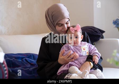 Mother holding kid looking at the camera feeling love with her baby wearing beautiful clothes celebrating eid Stock Photo