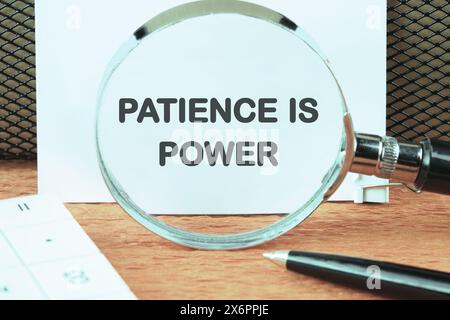 Concept words PATIENCE IS POWER through a magnifying glass on a white sheet Stock Photo