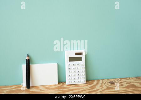 Calculator and memo pad, pencil on wooden desk. mint wall background Stock Photo