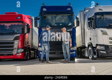 Two caucasian semi truck drivers shaking hands in front of a group of euro trucks. Stock Photo