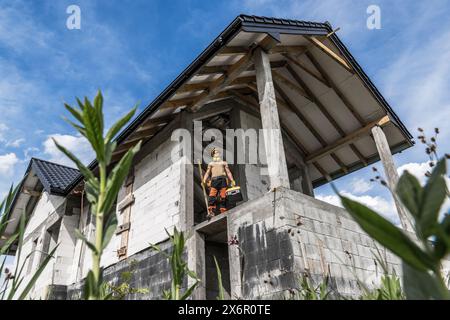 Caucasian Contractor worker stands on residential house in construction site. Stock Photo