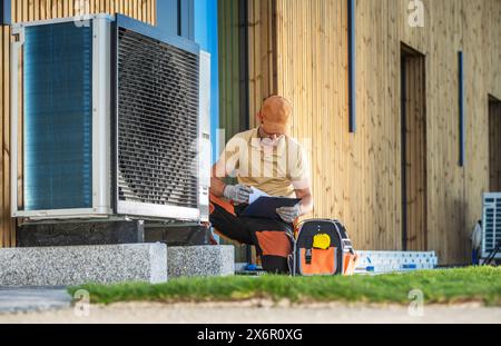 HVAC technician working on a modern heat pump in front of a building. Stock Photo