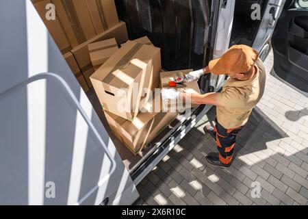 Courier loading cardboard boxes into a white cargo delivery van. Stock Photo