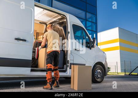 Courier standing by white moving van, opening door. Delivering packages to a client Stock Photo