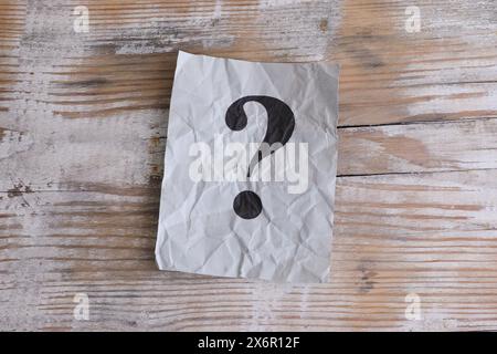 Gray crumpled paper note with question mark on it on a wooden background. Close-up. Stock Photo