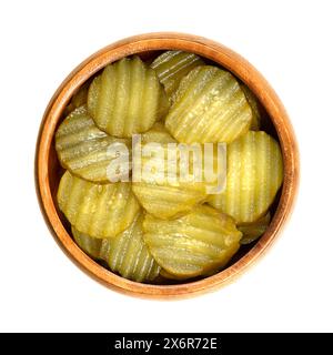 Burger gherkin slices, in a wooden bowl. Pickled cucumbers, cut in round and wavy form, pasteurized and preserved in vinegar brine, with spices. Stock Photo