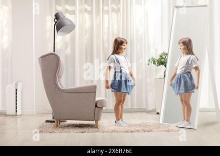 Little girl holding her skirt and looking into a mirror at home Stock Photo