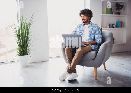 Photo of funky positive man wear checkered shirt working modern gadget staying home indoors house apartment room Stock Photo