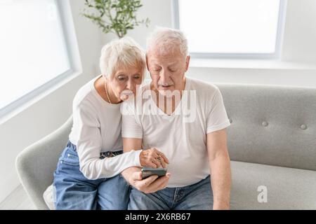 senior retired couple having great moment together on cozy sofa using cellphone Stock Photo