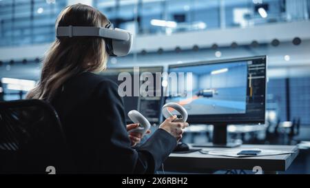 Industrial Software Developer Writing Code and Testing Automotive Manufacturing Interface. Engineer Editing Electric Motor and Car Chassis while Wearing Virtual Reality Headset and Using Controllers. Stock Photo