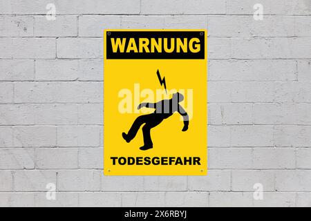 Yellow warning sign screwed to a brick wall to warn about a threat. In the middle of the panel, there is a man being electrocuted and the message in G Stock Photo