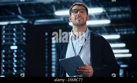 Male IT Specialist Walks Between Row of Operational Server Racks in Data Center. Engineer Uses Tablet Computer for Maintenance and Diagnostics in Cyber Security and Data Protection Facility. Stock Photo