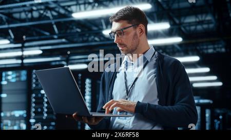 Successful Data Center IT Specialist Using Laptop Computer. Server Farm Cloud Computing Facility with System Administrator Working. Data Protection Engineering Network for Cyber Security. Stock Photo