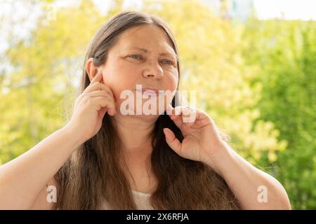 caucasian mature woman holds painful ear, hearing loss, face close-up, medical concept, hearing control, middle ear inflammation, Cochlear implant Stock Photo