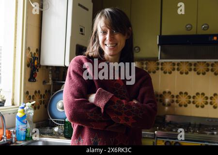 Portrait of An Adult Latin Woman in a red sweater is standing in a kitchen by the window. She is smiling and she is happy looking at camera. Stock Photo