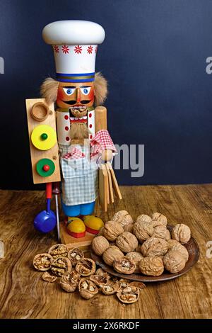 A colorful Nutcracker with a walnut in his mouth. Standing by a bowl with whole walnuts and shelled walnuts. Stock Photo
