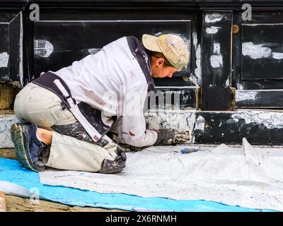 Young female decorator sanding shop front prior to repainting - Loches, Indre-et-Loire (37), France. Stock Photo