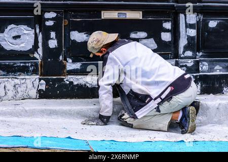 Young female decorator sanding shop front prior to repainting - Loches, Indre-et-Loire (37), France. Stock Photo
