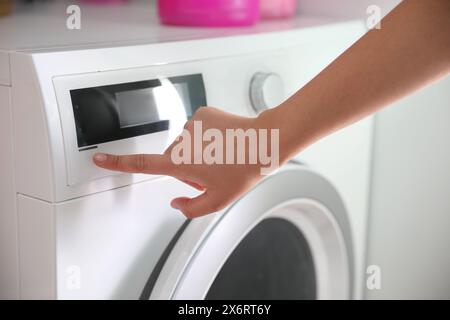 Woman pressing button on washing machine in bathroom, closeup Stock Photo