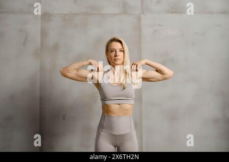 Strong fitness middle-aged woman showing her arms biceps at the gym Stock Photo