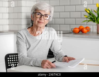 Woman With Grey Hair Is At Home, Sitting At Table With Documents Stock Photo