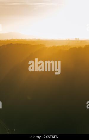 The sun shines through a gap in the clouds over a field with trees. Niederfell, Germany Stock Photo