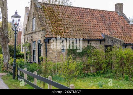 Rustic brick house with tiled roof and garden in spring, green vegetation and cosy atmosphere, historic houses in a small village with small streets Stock Photo