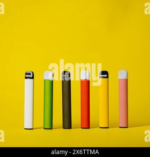 Set of colorful disposable electronic cigarettes with shadows on a yellow background. The concept of modern smoking, vaping and nicotine. Stock Photo