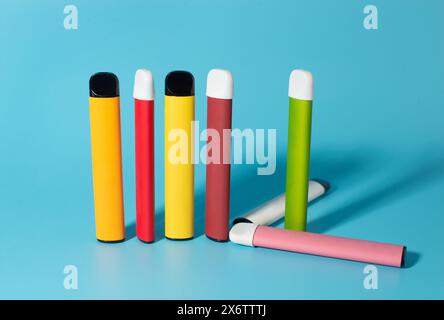 Set of colorful disposable electronic cigarettes with shadows on a blue background. The concept of modern smoking, vaping and nicotine. Top view. Stock Photo