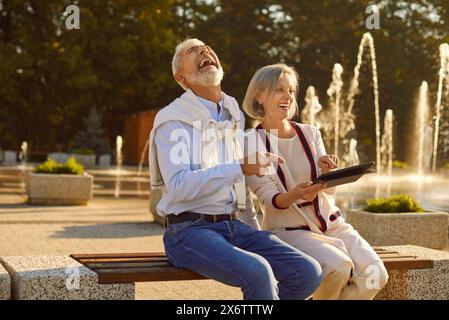 Senior Couple Using Digital Tablet and Laughing in the City Park Stock Photo