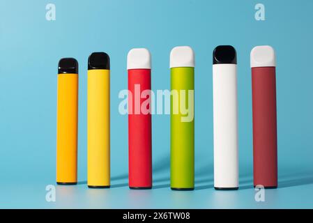 Set of colorful disposable electronic cigarettes with shadows on a blue background. The concept of modern smoking, vaping and nicotine. Top view. Stock Photo