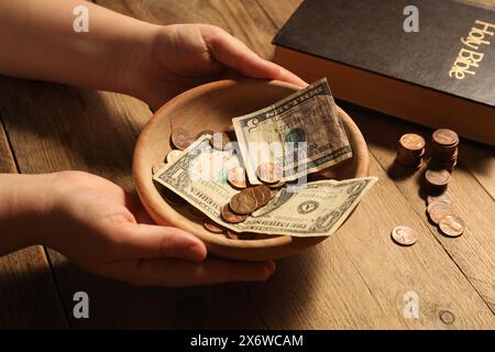 Donate and give concept. Woman holding bowl with money at wooden table, closeup Stock Photo