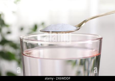 Spoon with baking soda over glass of water on blurred background, closeup Stock Photo