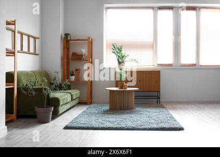 Green sofa, wooden round massive table and commode near white wall Stock Photo