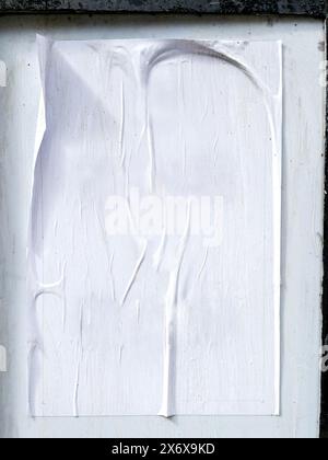 A wrinkled white poster pasted carelessly on a stone wall, showing signs of wear and weathering. Stock Photo