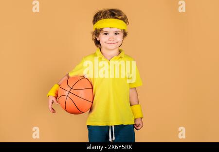 Little basketball player. Sporty kid boy in sportswear with basketball ball. Sport for children. Smiling child in sports uniform with ball. Concept of Stock Photo