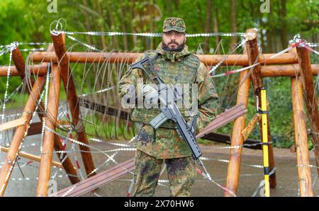 03 May 2024, Rhineland-Palatinate, Kirchheimbolanden: A Bundeswehr soldier secures access to an ammunition depot during an exercise. The Rhineland-Palatinate State Command is conducting an exercise with the Rhineland-Palatinate and Hunsrück homeland security companies to protect vital defense infrastructure on the site of the former ammunition depot near 'Kriegsfeld' (Donnersberg district). During the Bundeswehr exercise National Guardian, part of the Bundeswehr exercise series QUADRIGA, homeland security forces throughout Germany practise their core mission of protecting and securing vital de Stock Photo