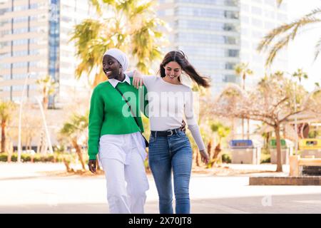 young multiracial couple of two women walking smiling happy through the city hugging, concept of diversity and modern lifestyle, copy space for text Stock Photo