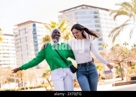 young multiracial couple of two women walking laughing happy and having fun through the city while hugging, concept of diversity and modern lifestyle, Stock Photo