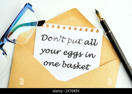 Don't put all your eggs in one basket text an inscription on a piece of paper peeking out of an envelope next to glasses and a pencil Stock Photo